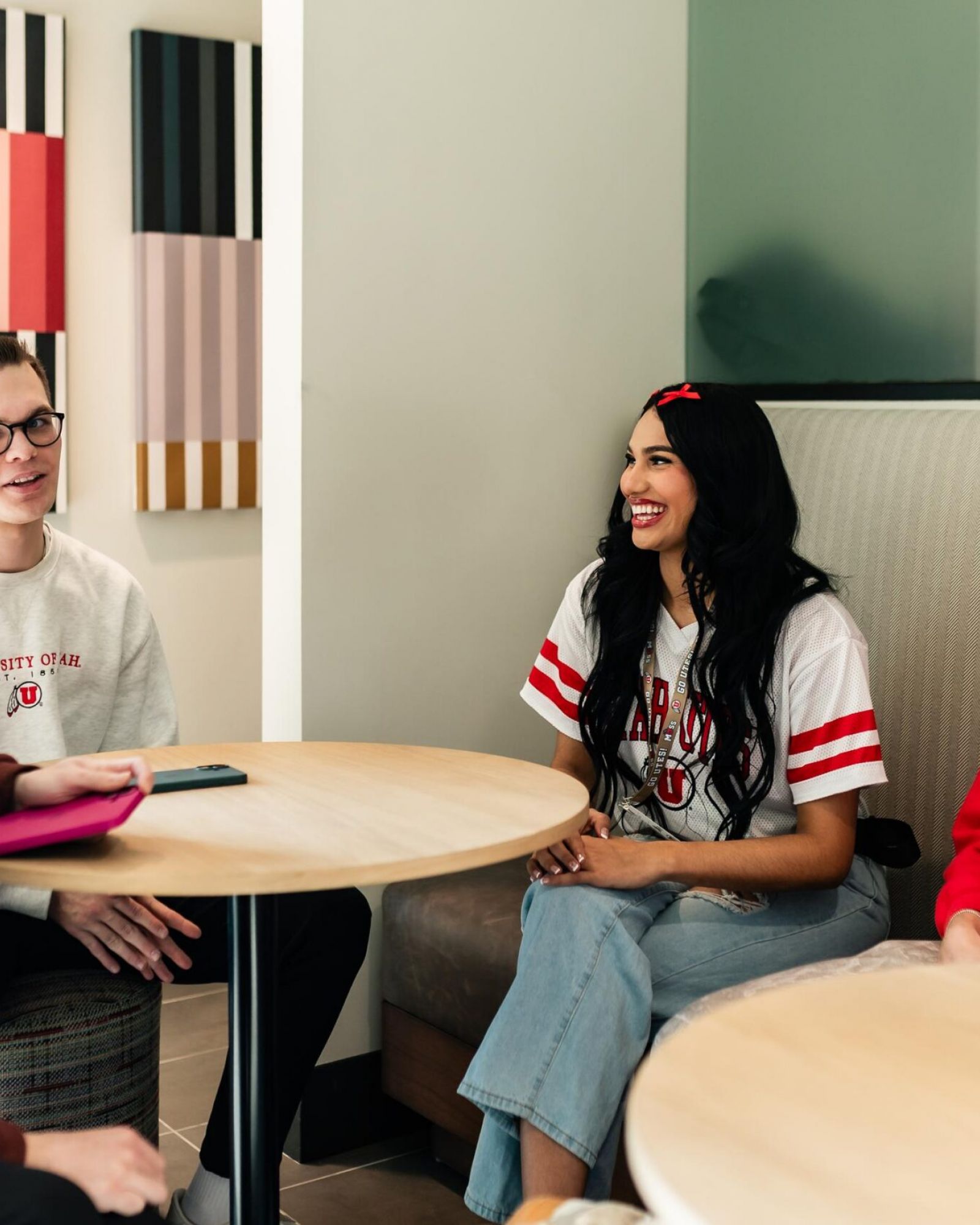 Montaire Student Living Apartments Four college students sit and talk around tables in a bright room, smiling and wearing university shirts.