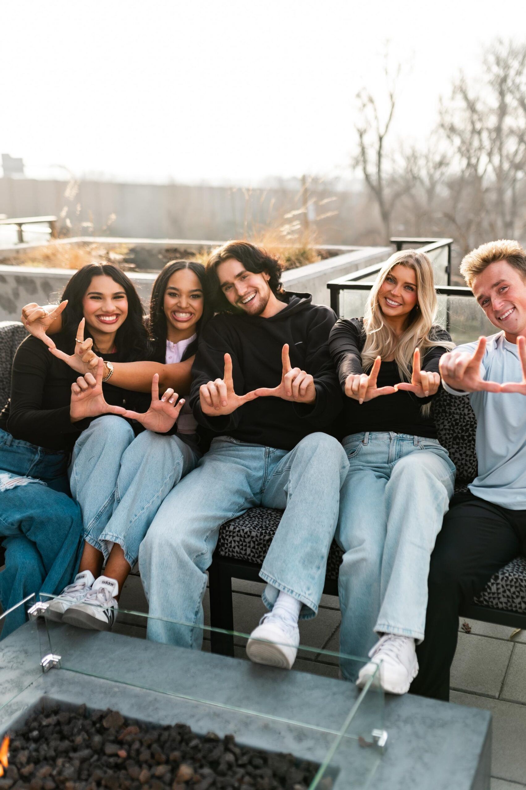 Montaire Student Living Apartments Five friends sit together outdoors on a patio, smiling and making "U" shapes with their hands.