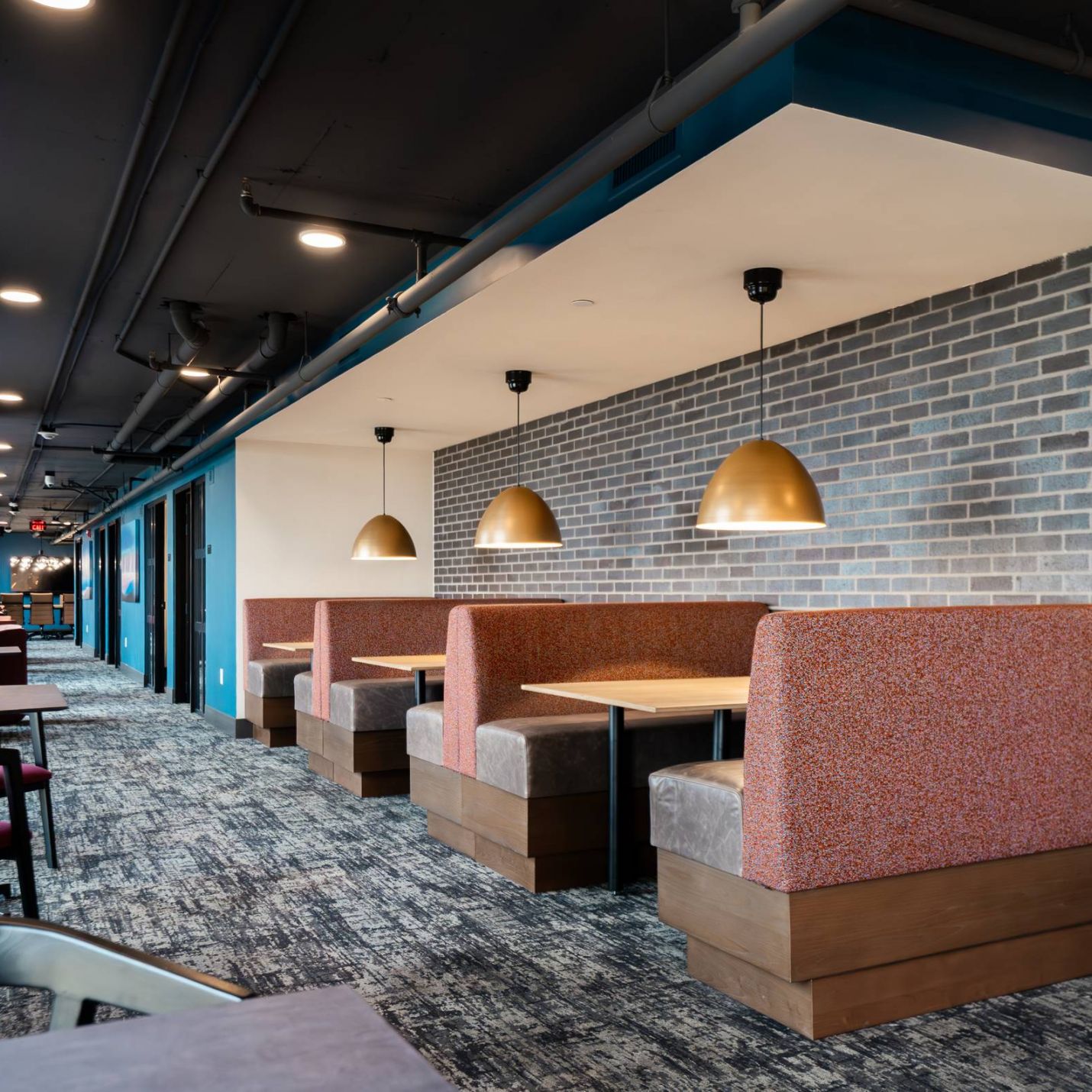 Montaire Student Living Apartments Modern restaurant booths with gold pendant lights, brick walls, and gray carpeted flooring.