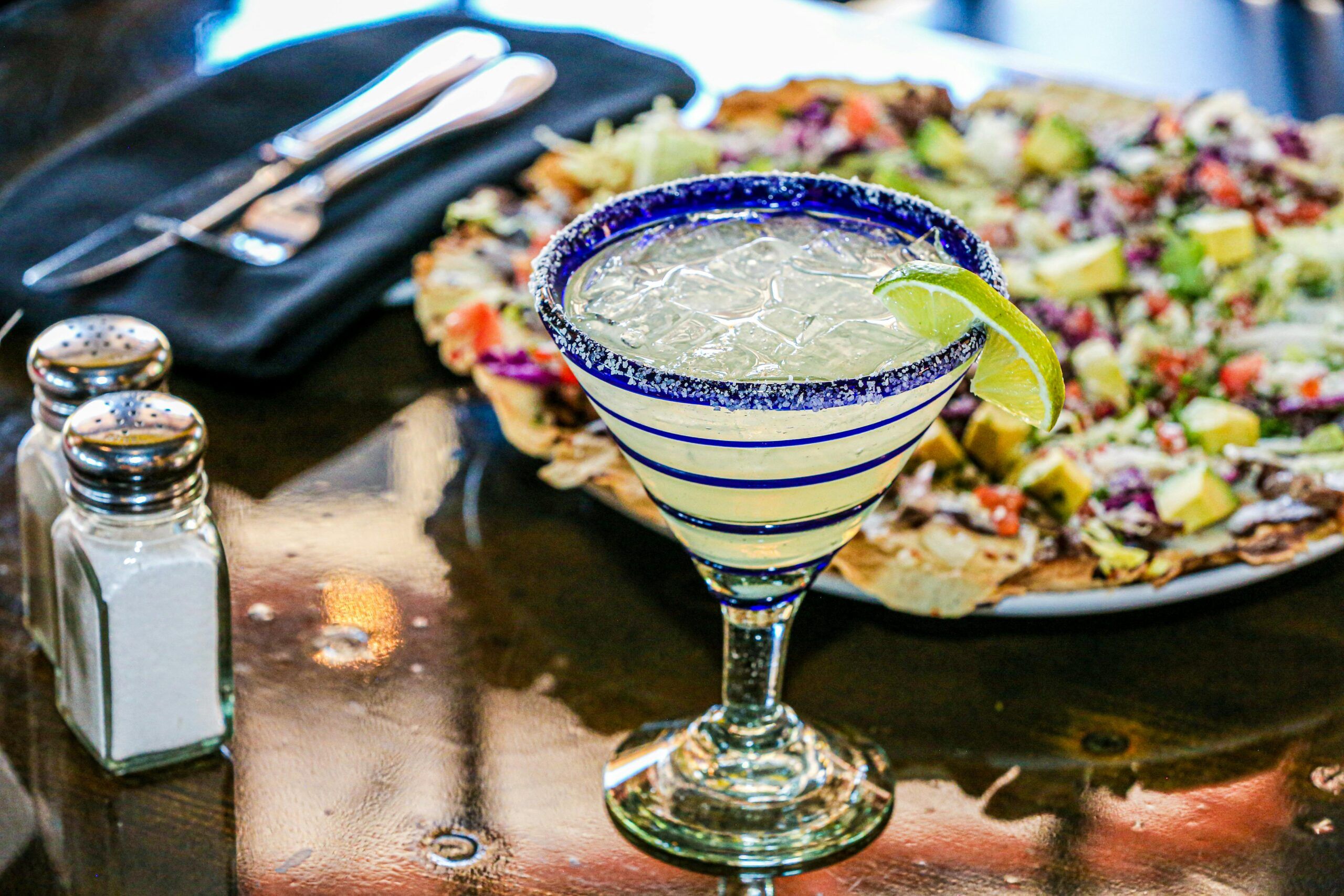 Montaire Student Living Apartments Margarita with lime on a table next to salt, pepper, utensils, and a plate of nachos with toppings.