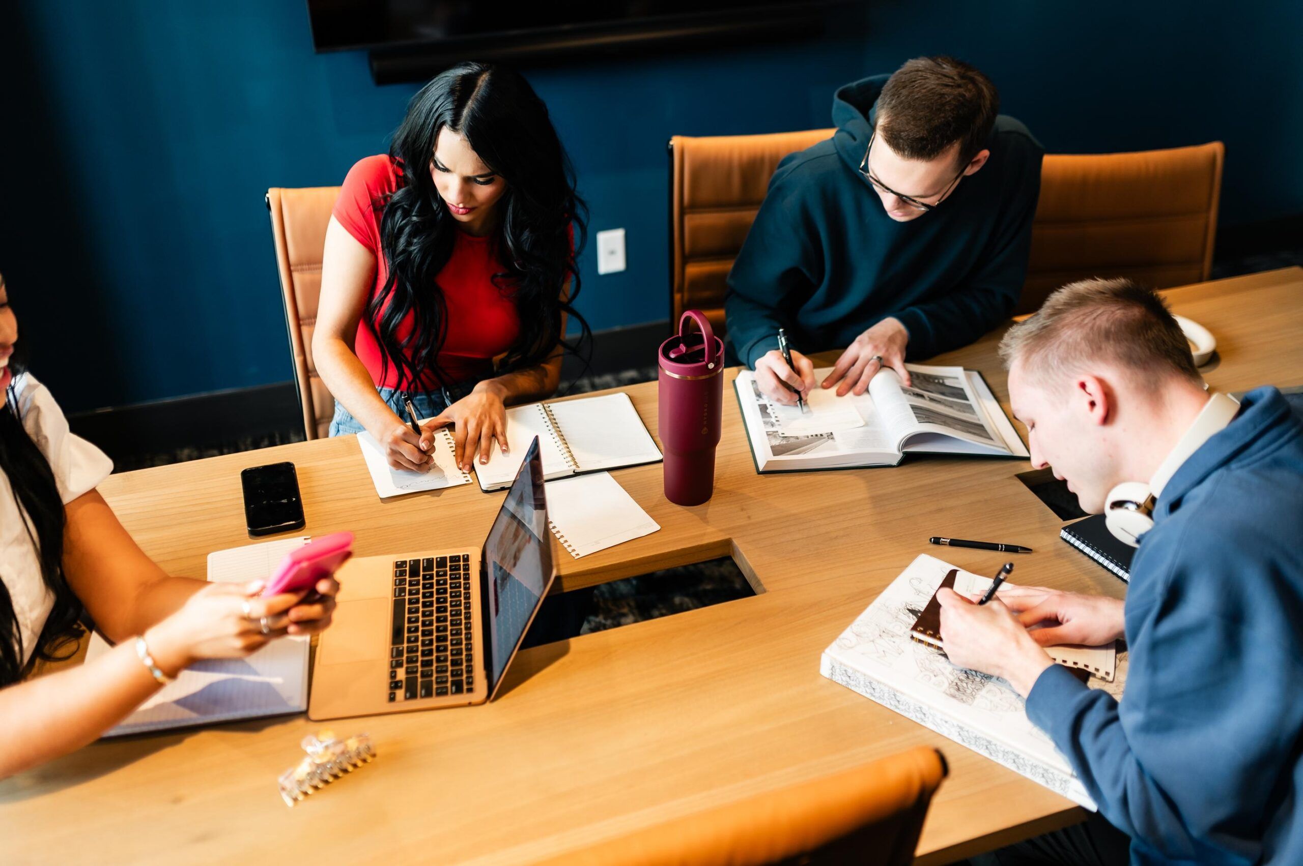 Montaire Student Living Apartments Four people sit at a table studying, writing in notebooks, and using laptops and books.