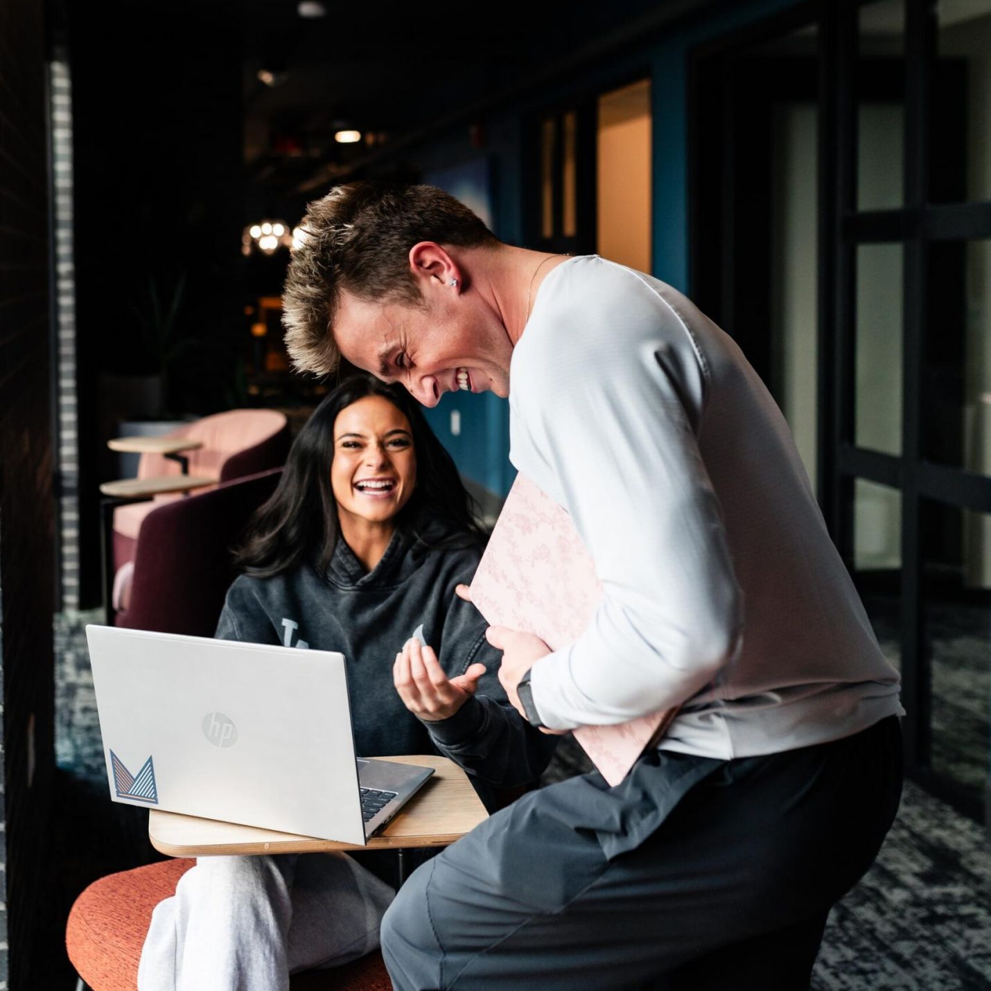 Montaire Student Living Apartments Two people smiling and talking in a modern lounge, with a laptop open on the table in front of them.