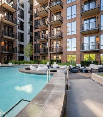 Montaire Student Living Apartments An outdoor swimming pool surrounded by a patio with lounge furniture and a multi-story brick apartment building.