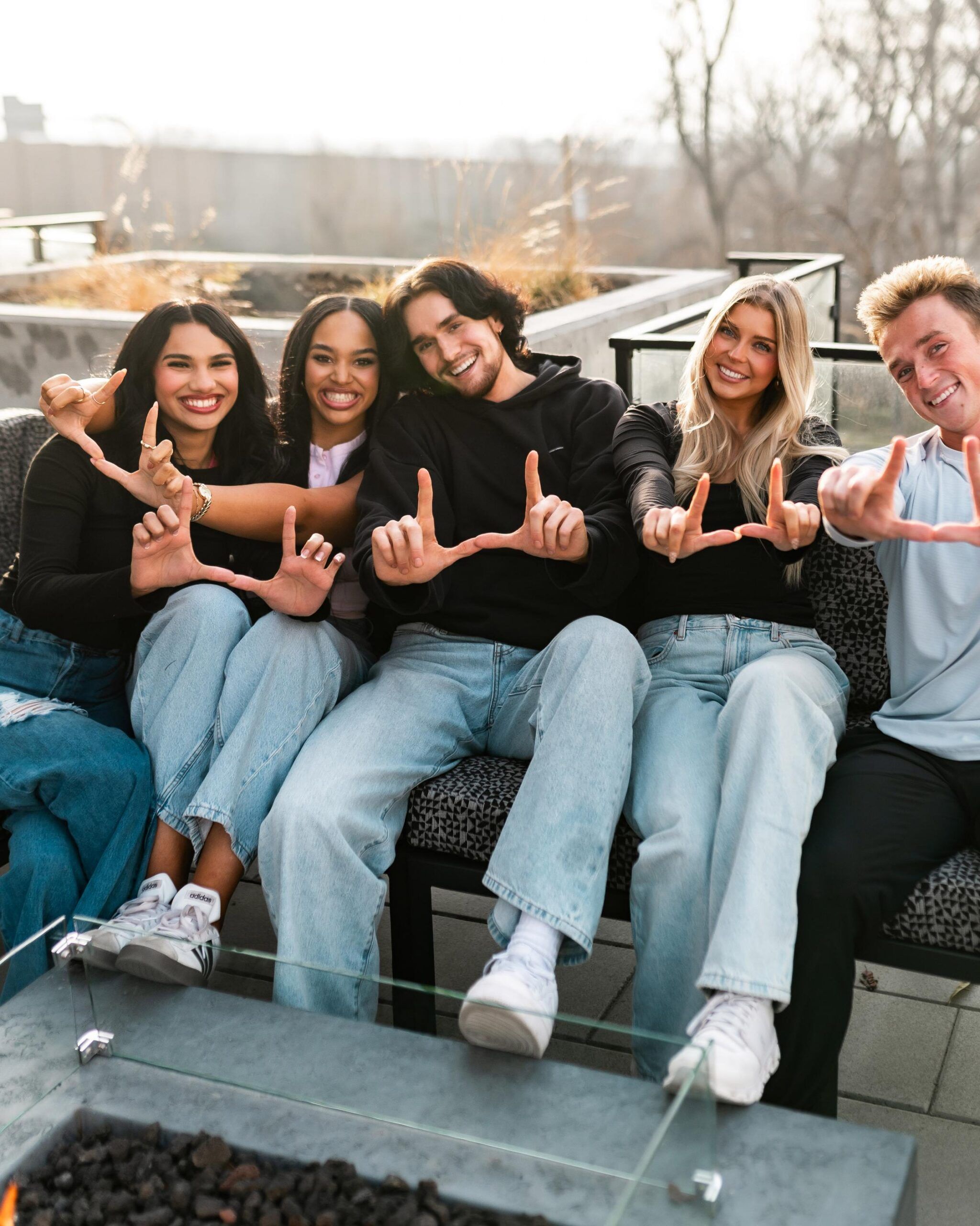 Montaire Student Living Apartments Five smiling young adults sitting outdoors, making "U" shapes with their hands toward the camera.