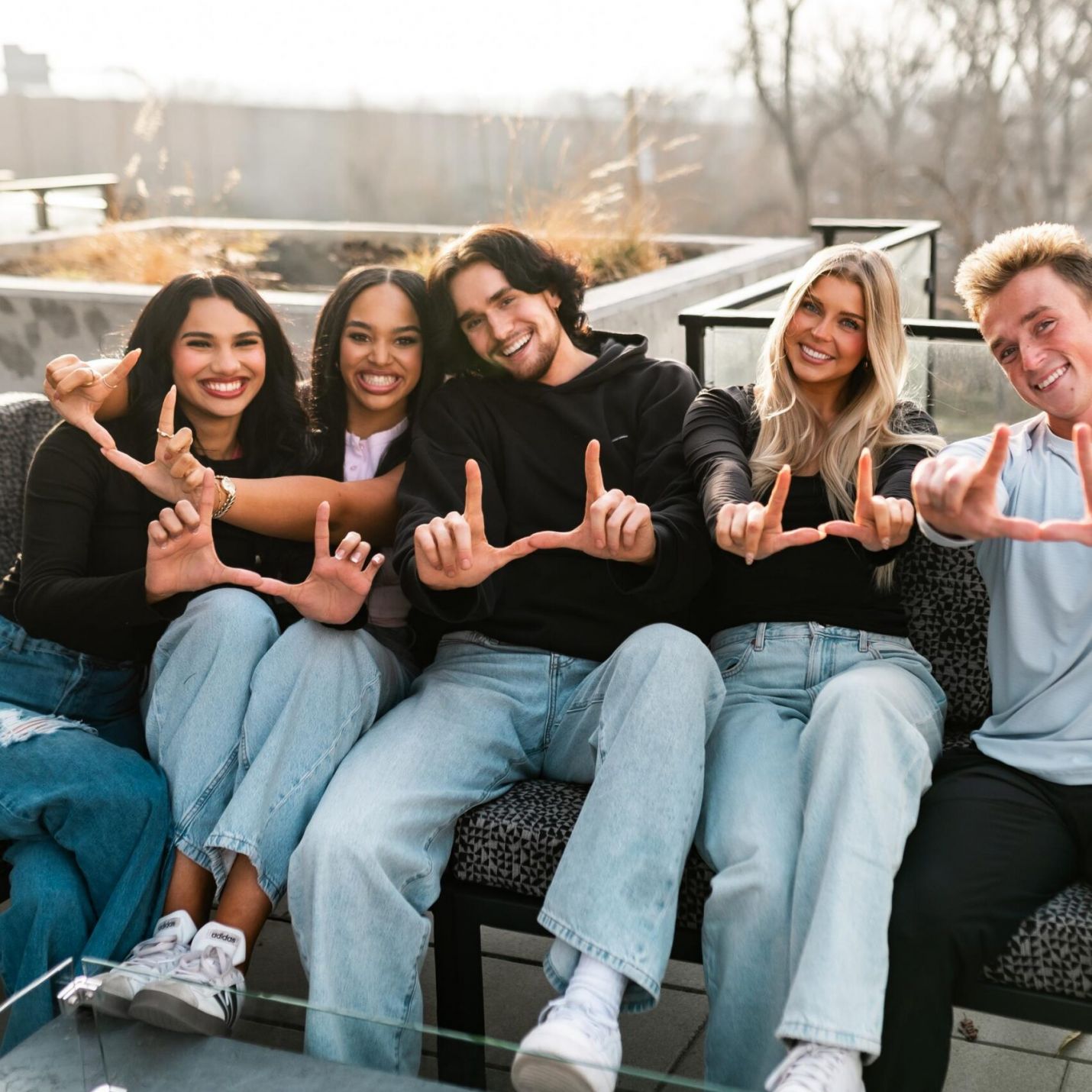 Montaire Student Living Apartments Five friends sit together outdoors on a patio, smiling and making "U" shapes with their hands.