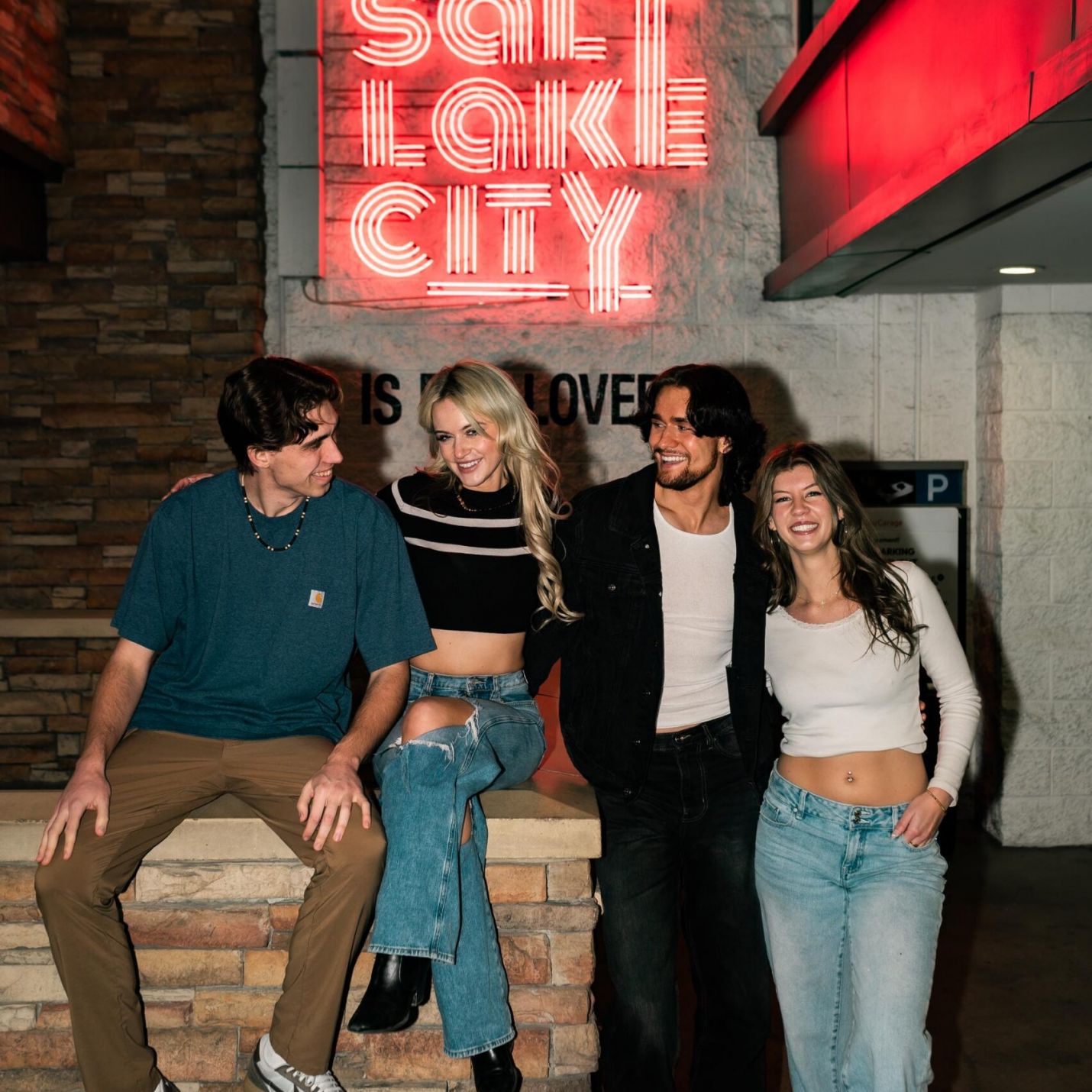 Montaire Student Living Apartments Four friends smiling and posing under a neon "Salt Lake City" sign at night.