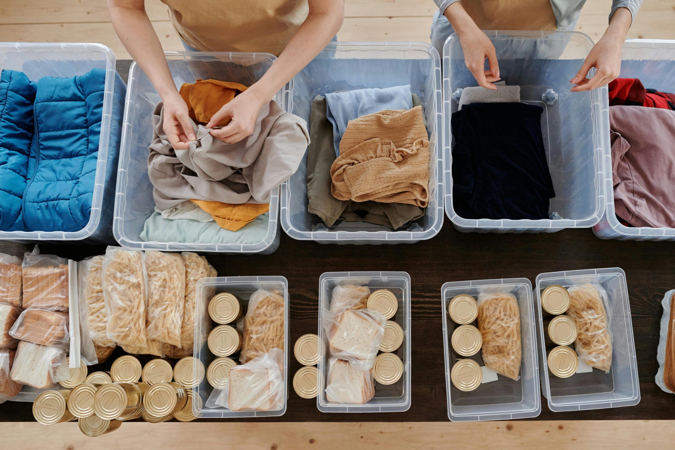 Montaire Student Living Apartments Two people sorting clothes and food items into plastic containers on a table, seen from above.
