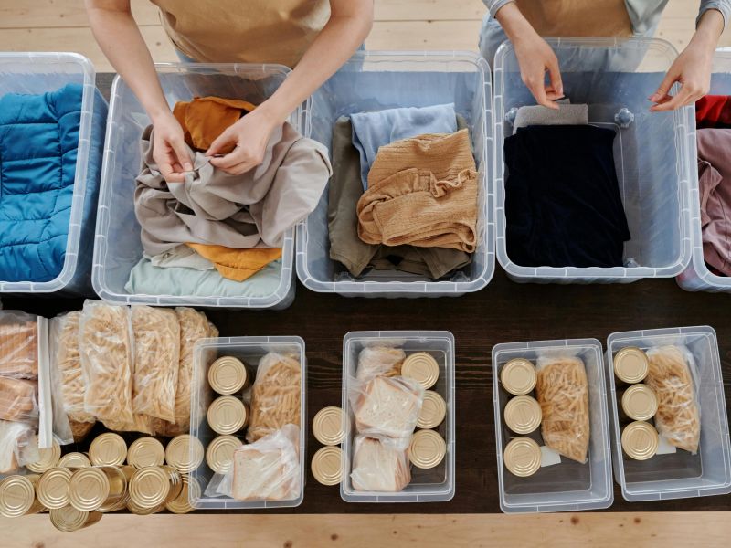 Montaire Student Living Apartments Two people sorting clothes and food items into plastic containers on a table, seen from above.