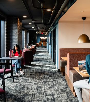 Montaire Student Living Apartments People working and studying in a modern lounge with booths, tables, and large windows letting in natural light.
