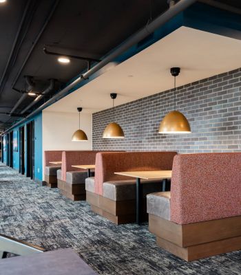 Montaire Student Living Apartments Modern restaurant booths with gold pendant lights, brick walls, and gray carpeted flooring.