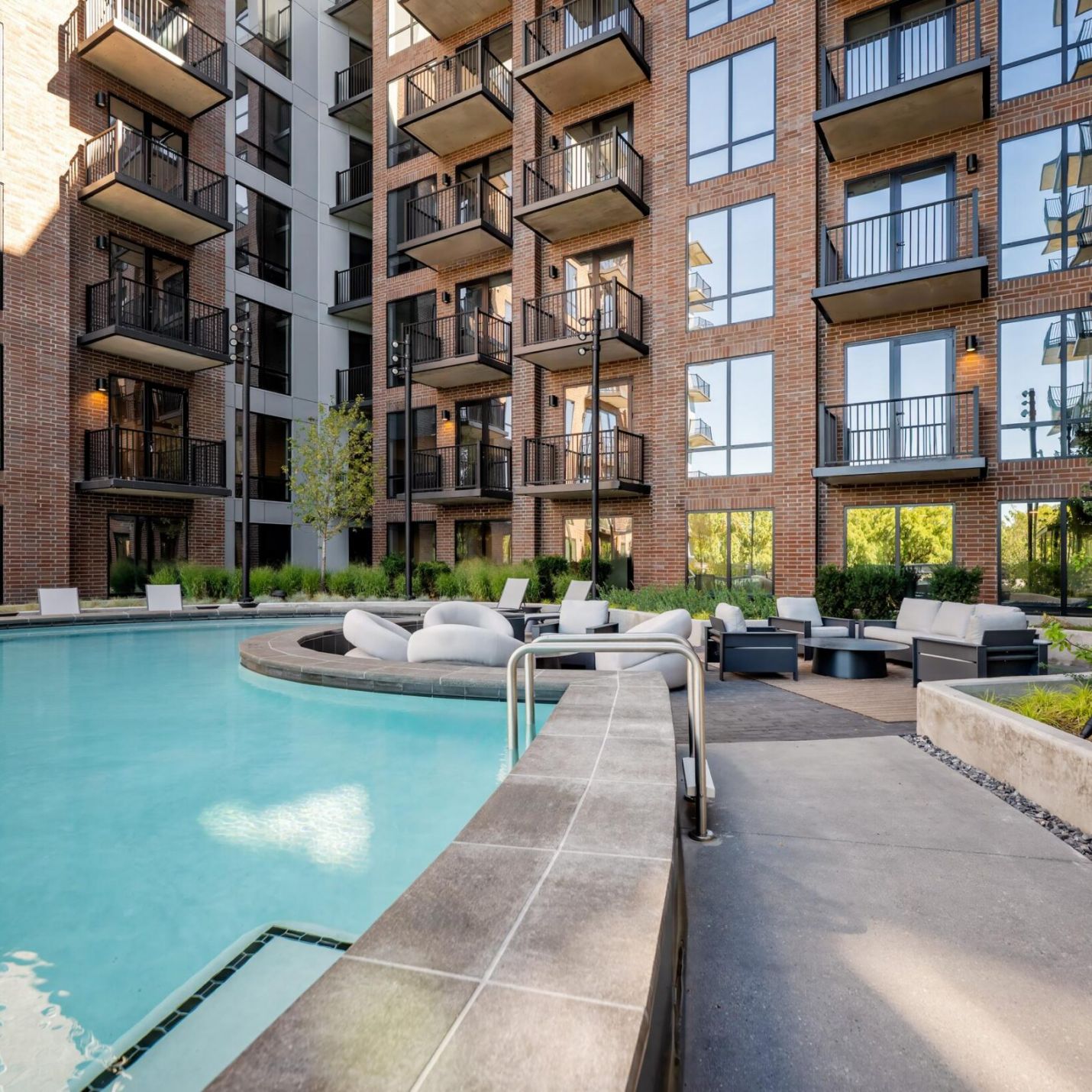 Montaire Student Living Apartments An outdoor swimming pool surrounded by a patio with lounge furniture and a multi-story brick apartment building.