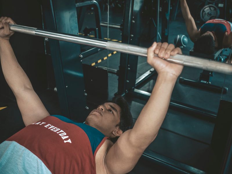 Montaire Student Living Apartments A person lies on a bench, gripping a barbell, preparing to lift weights in a gym.
