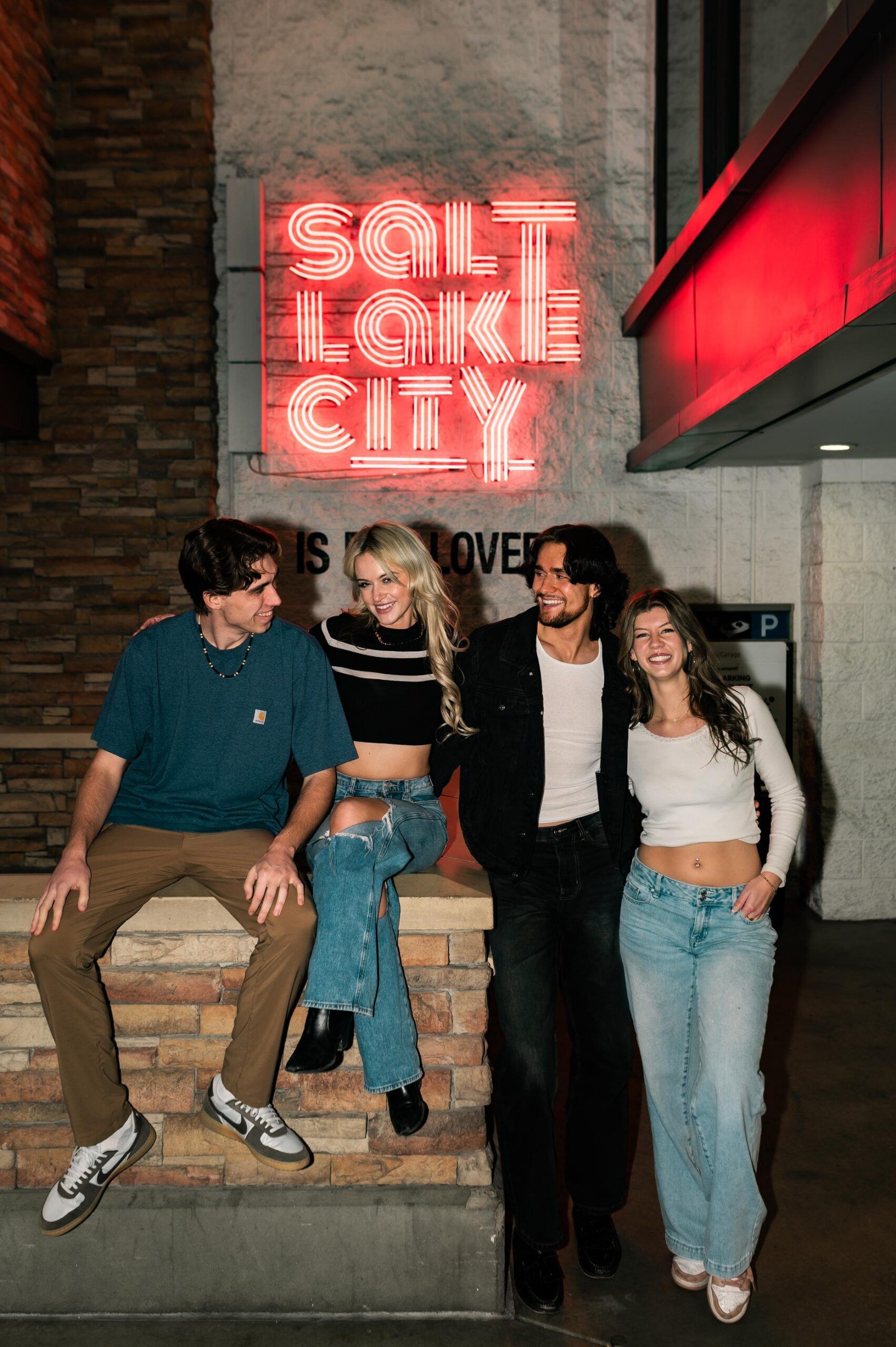Montaire Student Living Apartments Four friends smiling and posing under a neon "Salt Lake City" sign at night.