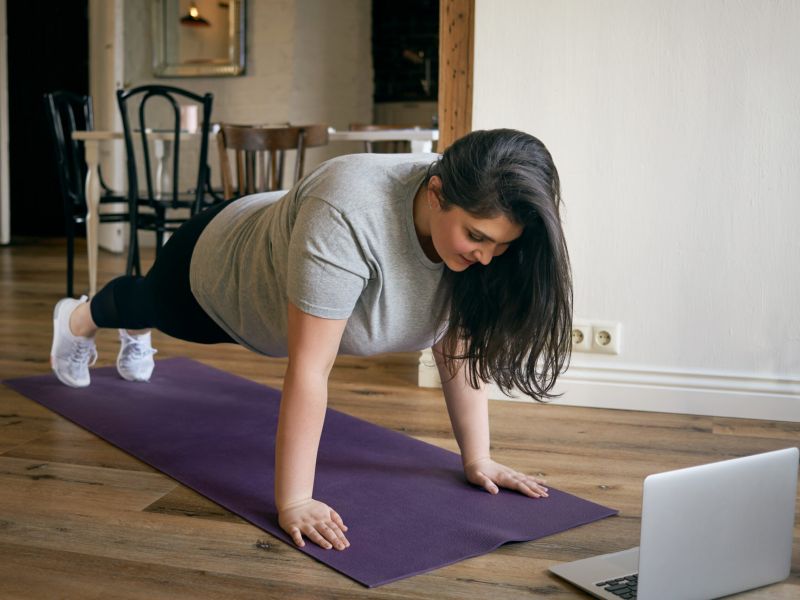 Montaire Student Living Apartments Woman doing a plank on a yoga mat at home, following a workout on a laptop.