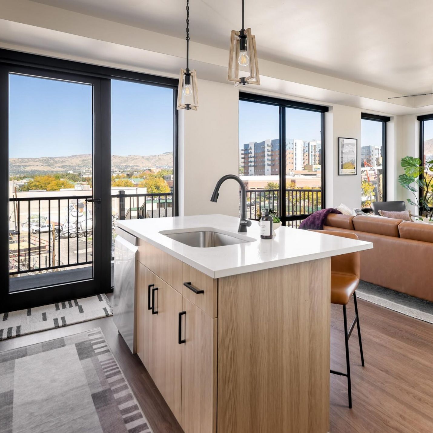 Montaire Student Living Apartments Modern kitchen with a wooden island and white countertop, overlooking a living room with floor-to-ceiling windows and mountain views.