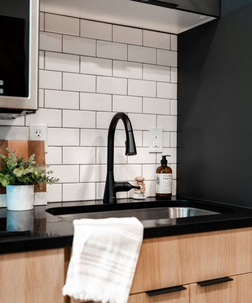Montaire Student Living Apartments Modern kitchen sink with a black faucet, white tile backsplash, soap dispenser, and potted plant.