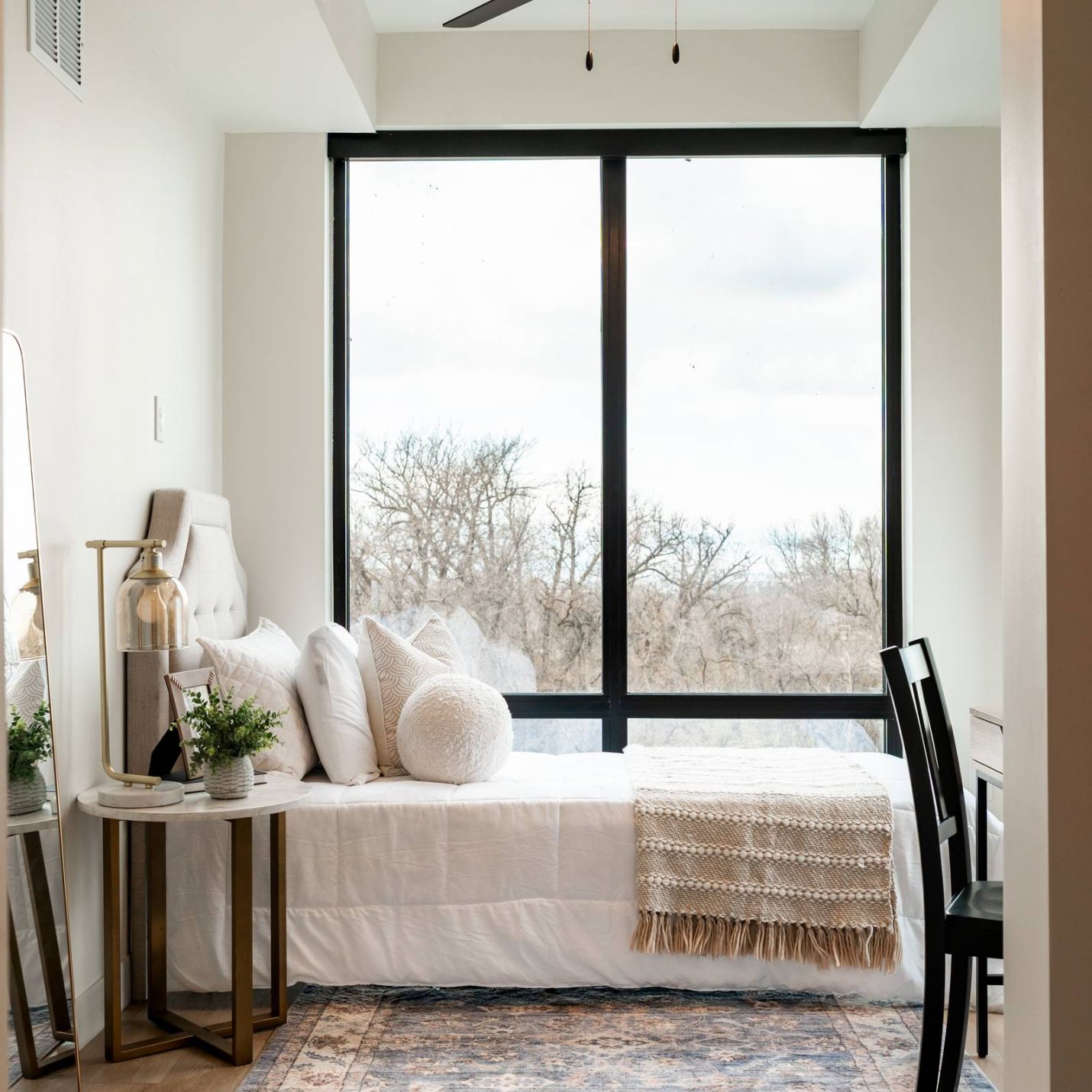Montaire Student Living Apartments Bright, modern bedroom with a daybed, large window, desk, and ceiling fan, decorated with neutral tones.