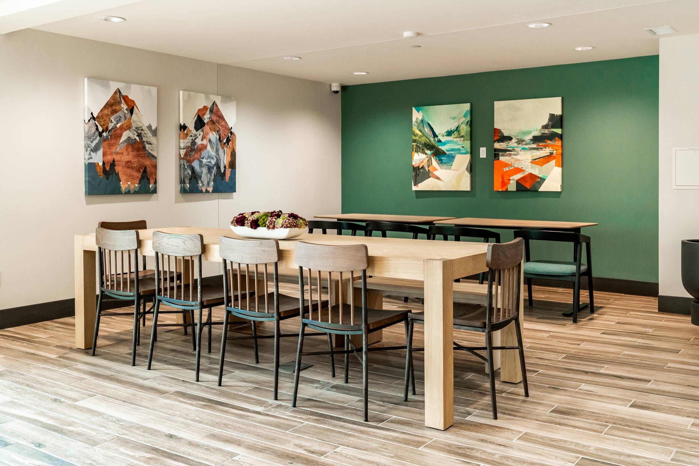 Montaire Student Living Apartments Modern dining area with wooden tables, mixed chairs, wall art, and a centerpiece on the main table.
