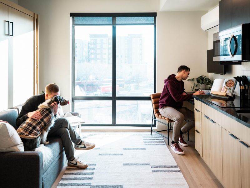 University of Utah Dorms. Montaire Student Living Apartments Two people in a modern apartment, one working at a kitchen counter, the other cuddling a dog on the couch.