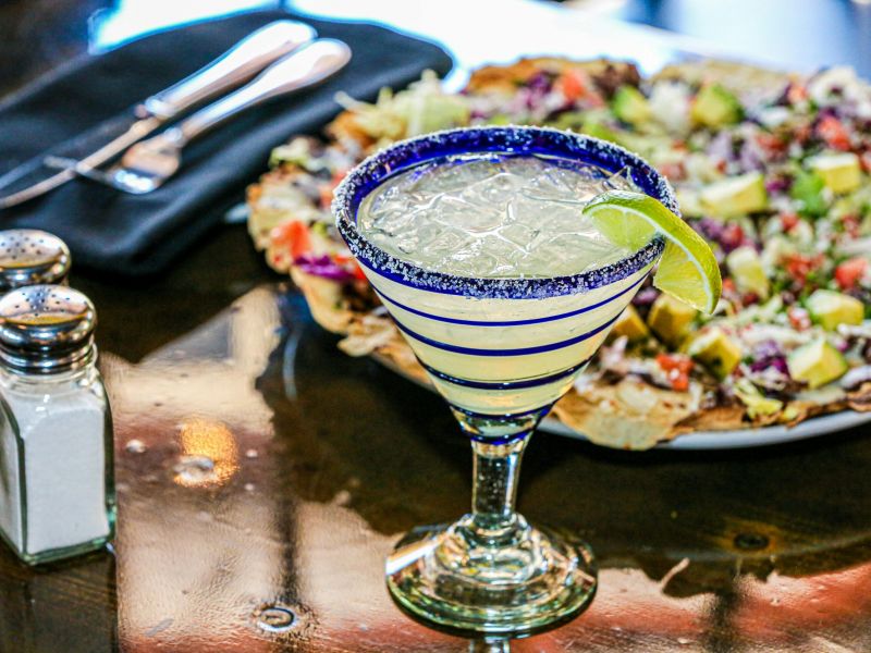 Montaire Student Living Apartments Margarita with lime on a table next to salt, pepper, utensils, and a plate of nachos with toppings.