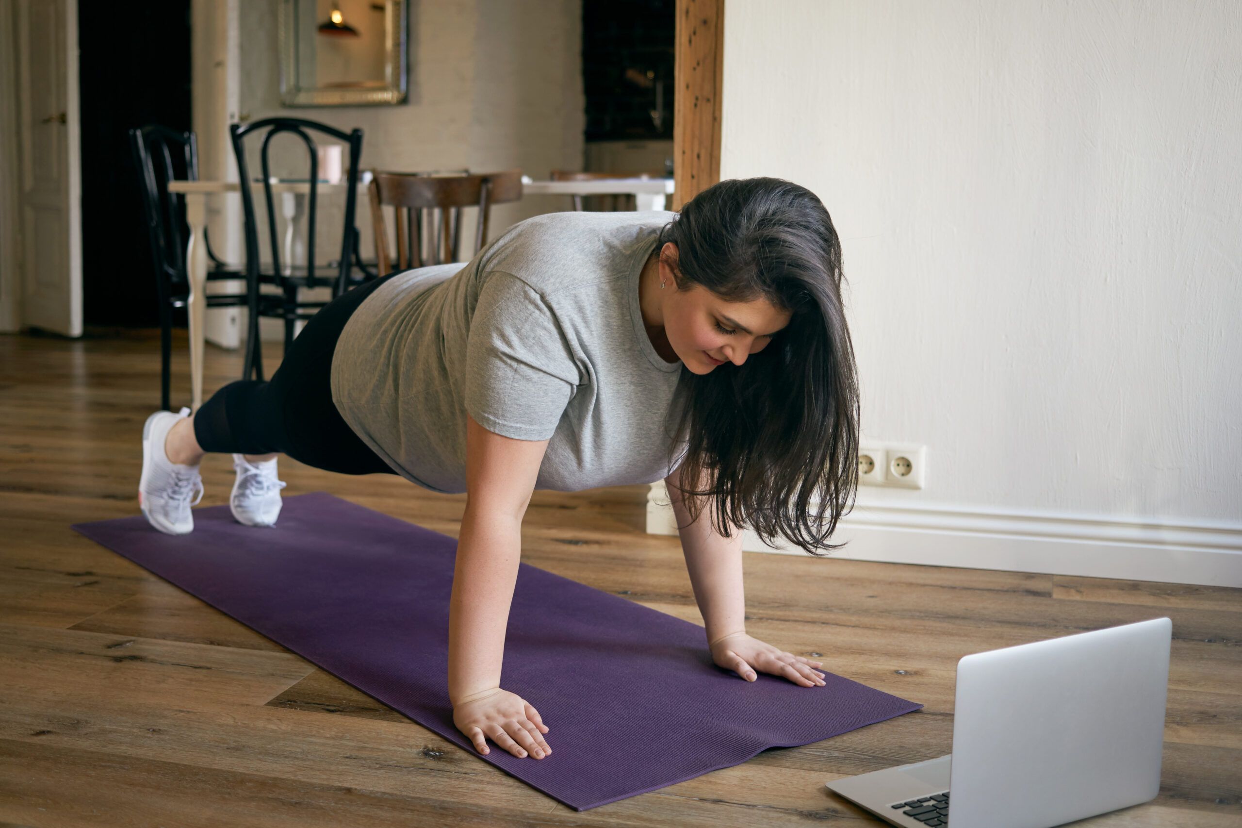 Montaire Student Living Apartments Woman doing a plank on a yoga mat at home, following a workout on a laptop.