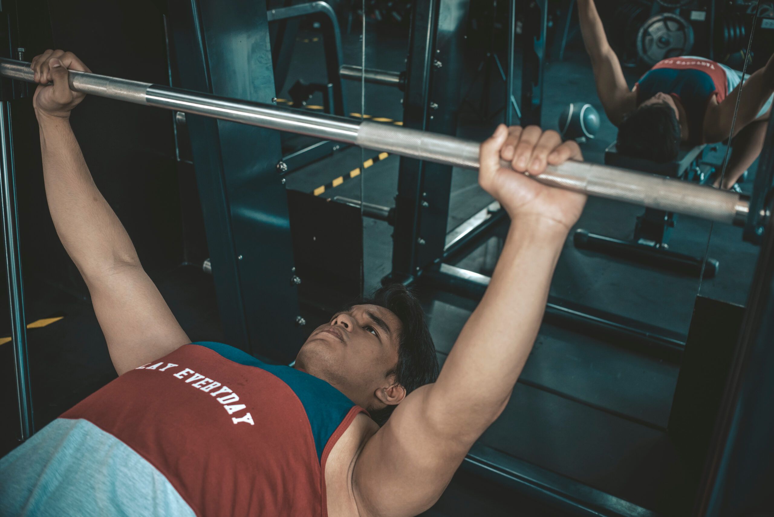 Montaire Student Living Apartments A person lies on a bench, gripping a barbell, preparing to lift weights in a gym.
