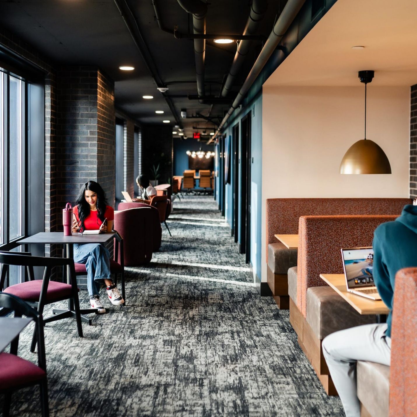 Montaire Student Living Apartments People working and studying in a modern lounge with booths, tables, and large windows letting in natural light.