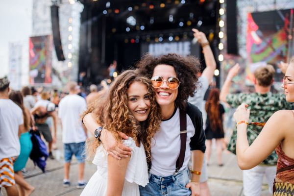 Montaire Student Living Apartments Two young women smiling and posing together at an outdoor music festival with a crowd in the background.