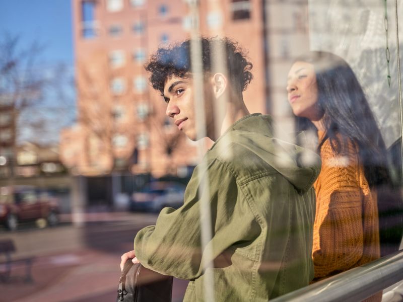 Montaire Student Living Apartments Two people stand by a window, looking outside with thoughtful expressions; city buildings are visible.